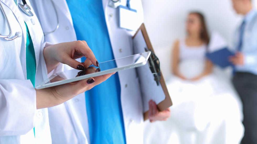 healthcare professional uses tablet next to other healthcare professional holding a clipboard