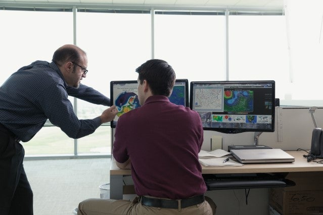 two people work on something at a computer desk